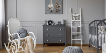 Pouf and rocking chair in grey baby's bedroom interior with ladder next to cabinet. Real photo